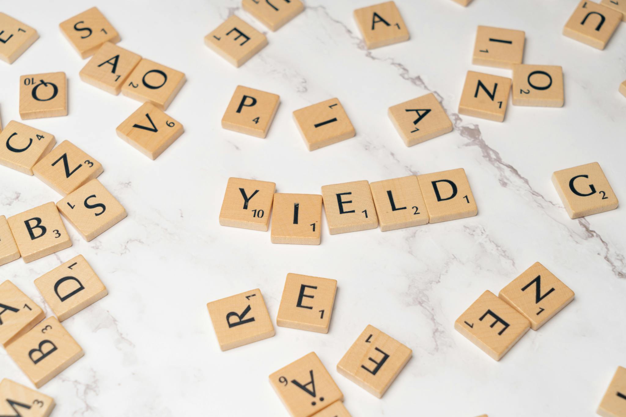 Scrabble tiles forming the word 'YIELD' on a marble surface, symbolizing finance and investment.